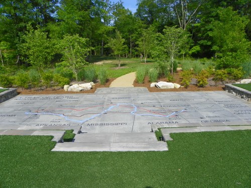 A landscaped area featuring engraved stone slabs with state names and a winding blue and red line, surrounded by greenery.