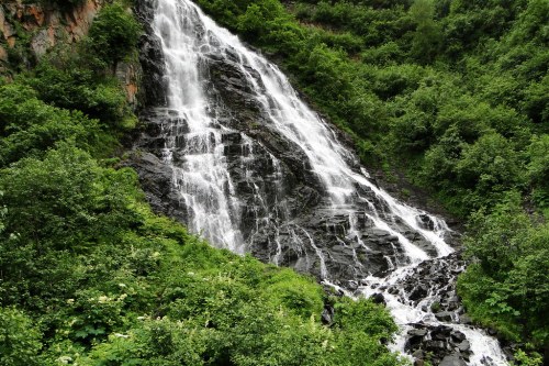 A cascading waterfall flows down rocky terrain, surrounded by lush green foliage and vibrant vegetation.