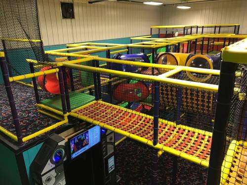 Colorful indoor play structure with tunnels and climbing areas, surrounded by safety netting and a vibrant carpet.