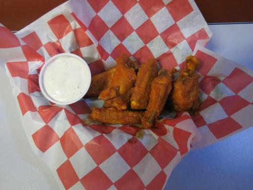 A basket of crispy chicken wings with a side of ranch dressing, served on red and white checkered paper.