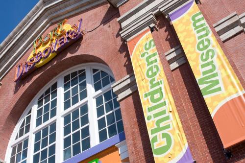 Exterior of Port Discovery Children's Museum, featuring colorful banners and a large window under a clear blue sky.
