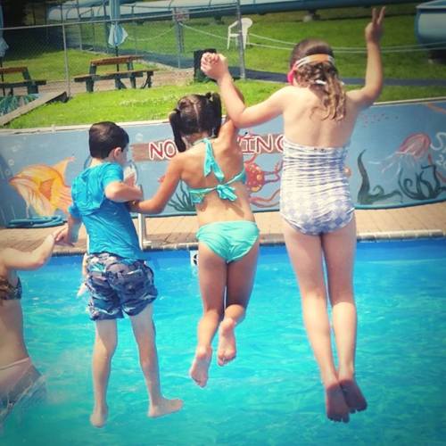 Children jumping into a swimming pool on a sunny day, enjoying a fun summer activity.