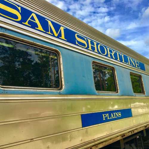 Side view of a train car with "SAM SHORTLINE" and "PLAINS" written on it, set against a blue sky.