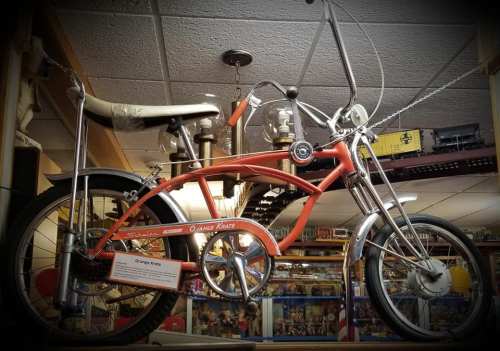 A vintage orange bicycle displayed in a museum, featuring a unique design and chrome accents.
