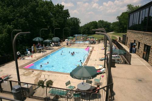 Aerial view of a pool area with people swimming, lounge chairs, umbrellas, and a building in the background.