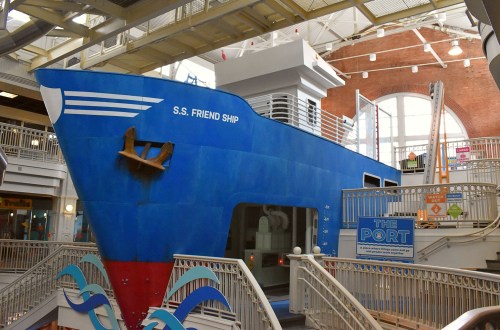 A large blue ship model, named S.S. Friend Ship, is displayed indoors with stairs and railings around it.