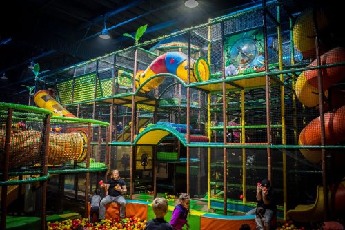 A colorful indoor playground with slides, tunnels, and a ball pit, filled with children playing and exploring.