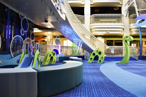 Colorful indoor playground with slides and dinosaur-shaped structures, featuring a modern design and soft flooring.