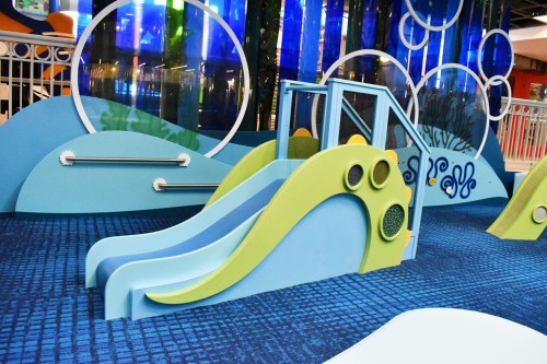 Colorful indoor playground featuring a blue and green slide with ocean-themed decor and soft flooring.