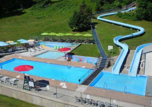 Aerial view of a pool area featuring two swimming pools, water slides, lounge chairs, and umbrellas on a sunny day.