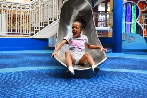 A joyful child slides down a shiny metal slide in a colorful indoor play area, smiling and having fun.