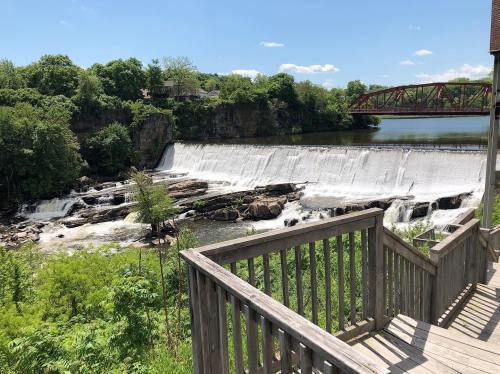 A scenic view of a waterfall with a wooden railing in the foreground and a bridge in the background under a clear blue sky.