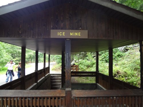 A wooden structure labeled "ICE MINE" surrounded by greenery, with two people walking nearby.