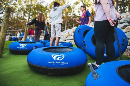 A group of people stands near blue inflatable tubes at Wolfe Mountain, surrounded by trees and rocky terrain.