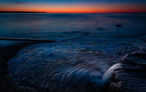 A serene seascape at dusk, with gentle waves flowing over rocks against a colorful sunset sky.