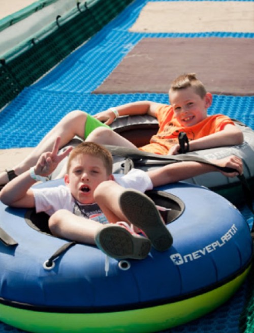 Two boys sitting in inflatable tubes, smiling and posing for the camera on a blue surface.