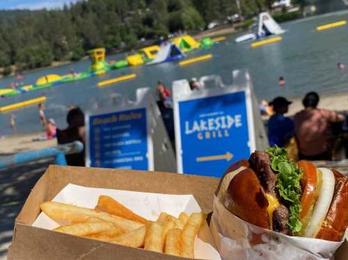 A close-up of a burger and fries with a lake and inflatable water park in the background on a sunny day.