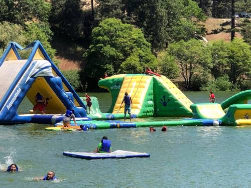 A vibrant inflatable water park with people playing and swimming in a lake surrounded by trees.
