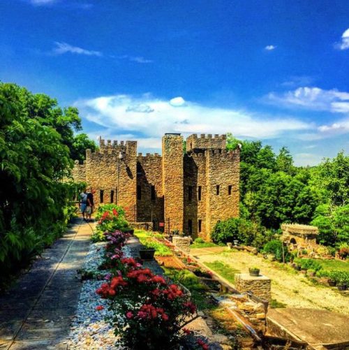 A stone castle surrounded by lush greenery and colorful flowers under a bright blue sky.