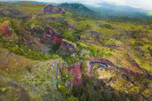 Aerial view of a lush, volcanic landscape with colorful ridges and greenery, showcasing rugged terrain and distant hills.