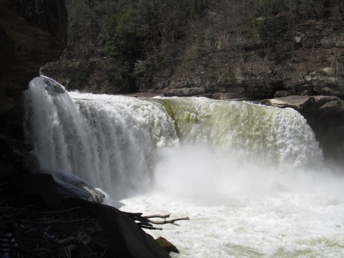 A powerful waterfall cascades over rocky cliffs, creating mist and a serene natural landscape.
