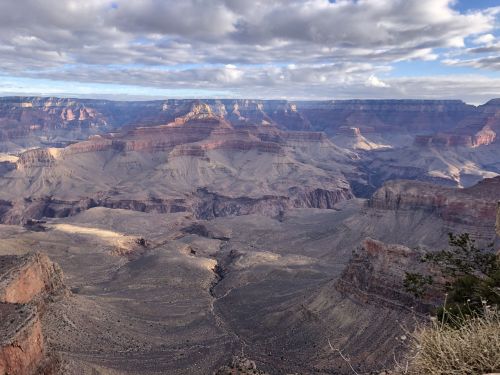 A panoramic view of the Grand Canyon, showcasing layered rock formations and dramatic cliffs under a cloudy sky.