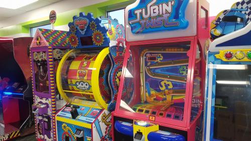 Colorful arcade games featuring a spinning wheel and a ticket redemption machine in a bright gaming area.