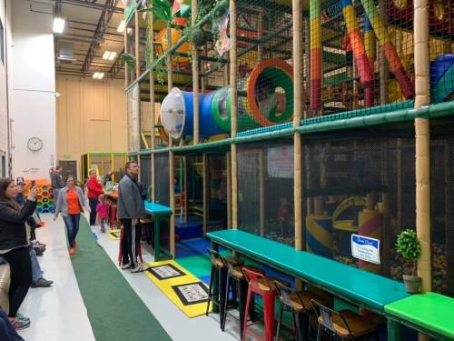 A colorful indoor play area with climbing structures, slides, and seating for parents observing children playing.