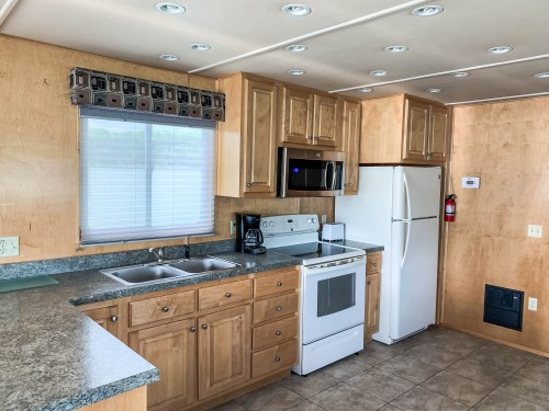 A modern kitchen with wooden cabinets, a window, stainless steel appliances, and a tiled floor.