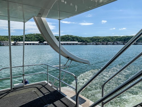 View from a boat showing a water slide and steps, with a scenic lakeside landscape in the background.