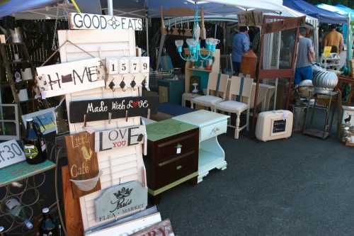 A vibrant flea market scene with various vintage signs and furniture for sale under colorful tents.