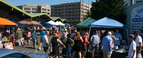 A bustling outdoor market with colorful tents, vendors, and a crowd of people enjoying the sunny day.