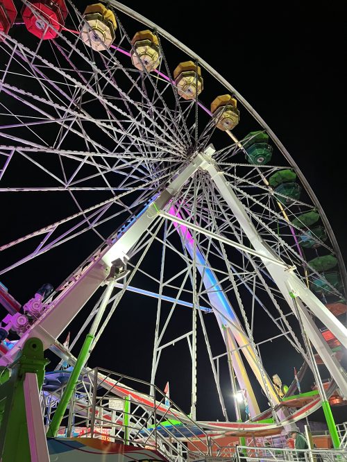 A brightly lit Ferris wheel at night, showcasing colorful gondolas against a dark sky.