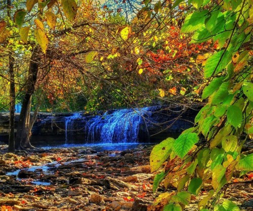 A serene waterfall surrounded by vibrant autumn leaves and rocky terrain, capturing the beauty of nature.
