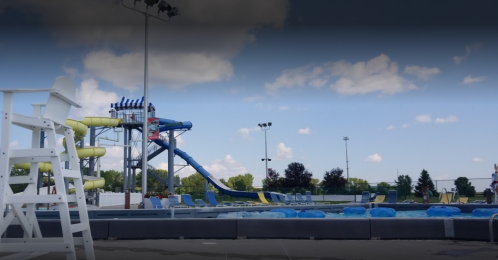 A water park featuring a large slide, a swimming pool, and lounge chairs under a blue sky with clouds.