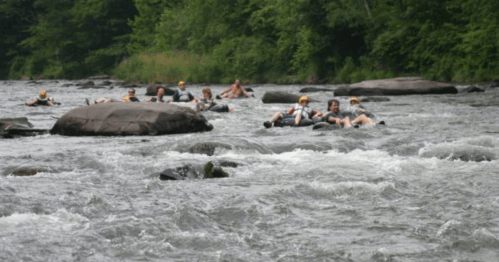 A group of people tubing down a river, navigating around rocks with lush greenery in the background.