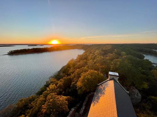A sunset over a calm lake, with lush green trees lining the shore and a rooftop in the foreground.