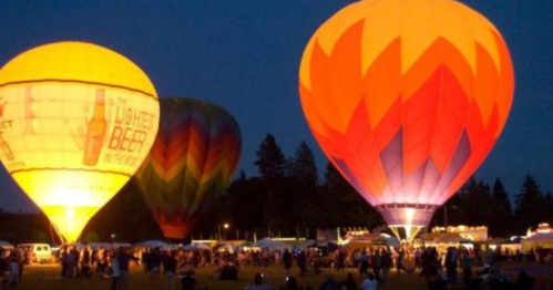 Colorful hot air balloons illuminated at night, surrounded by a crowd and festive atmosphere.