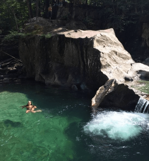 A person swims in a clear, turquoise pool surrounded by rocky cliffs and lush greenery.
