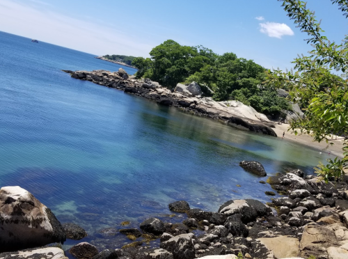 A serene coastal scene with clear blue water, rocky shorelines, and lush greenery under a bright sky.