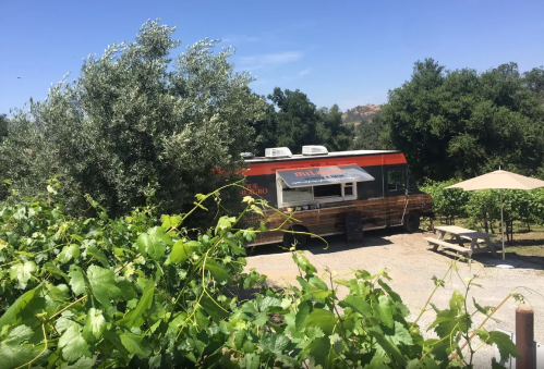 A food truck parked among green vines and trees under a clear blue sky.
