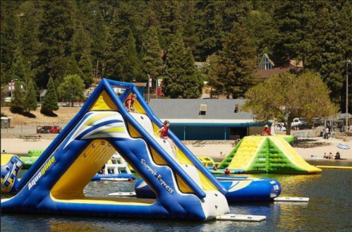 Colorful inflatable water structures on a lake, with people playing and trees in the background.
