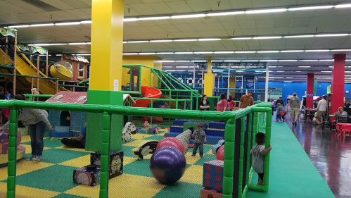 A colorful indoor play area with children playing on equipment, climbing structures, and soft play items.