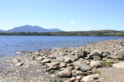 A serene lakeside view with rocky shorelines and distant mountains under a clear blue sky.