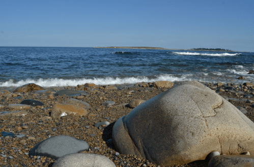A rocky beach with smooth stones, gentle waves, and a clear blue sky in the background.