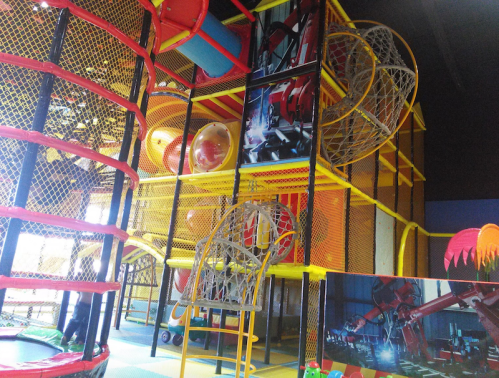Colorful indoor play structure with slides, tunnels, and climbing areas, surrounded by safety netting.