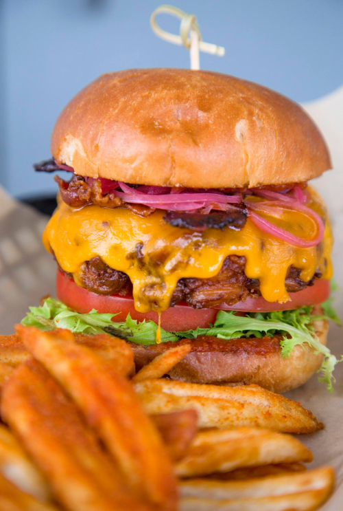 A juicy cheeseburger with melted cheese, lettuce, tomato, and pickled onions, served with crispy sweet potato fries.