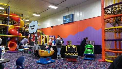 A colorful indoor play area with climbing structures, arcade games, and children playing in a vibrant, fun environment.