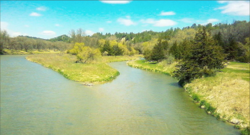 A winding river flows through a lush green landscape with trees and blue skies in the background.