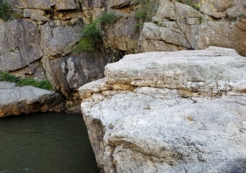 A rocky cliff edge overlooking a calm green river surrounded by rugged terrain.